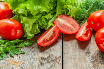 vegetables for a salad: fresh crispy lettuce, juicy ripe tomatoes and herbs on a wooden table, vegan food concept
