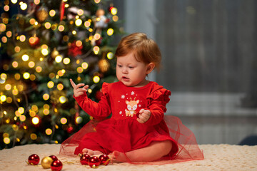 Little girl with red hair in a red New Year's dress on the background of a Christmas tree at home