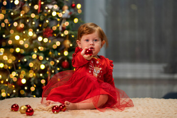 Little girl with red hair in a red New Year's dress holding a Christmas tree toy