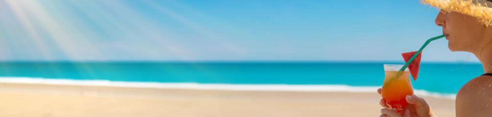 A woman holds a cocktail in her hand against the background of the sea. Selective focus.