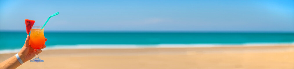 A woman holds a cocktail in her hand against the background of the sea. Selective focus.