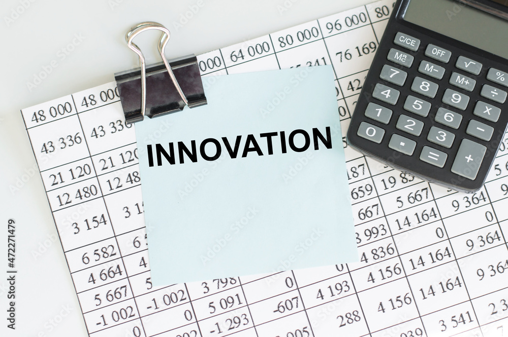 Aufkleber text innovation on blue paper for notes on a clip with a sheet of reports on the table next to the c