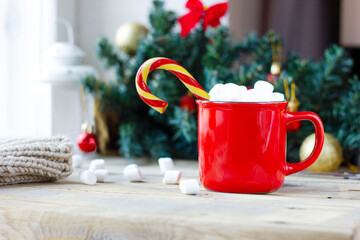 Obraz na płótnie Canvas cozy winter hot chocolate drink with marshmallows and lollipop in red mug on background of christmas decor, cute bright card with hot milk in a mug on a wooden background
