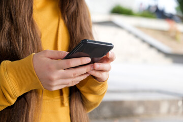 A girl with long hair holds a smartphone close-up.