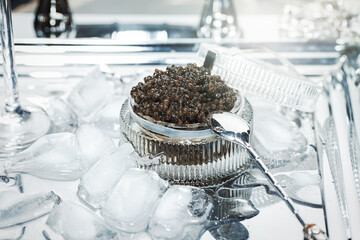 Black caviar. Black sturgeon caviar in a cut-glass bowl and a metal spoon on a silver tray filled with ice.