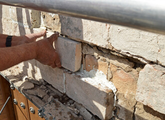 Albañil constructor colocando ladrillos de taco en un muro con mortero de cal. Trabajos de...
