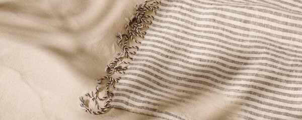 Striped linen beach towel with fringes on sandy beach with shadows from palm tree. Relaxation and...