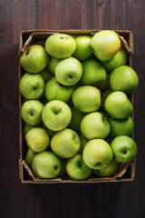 Ripe and juicy Green apples in a box on a wooden table.