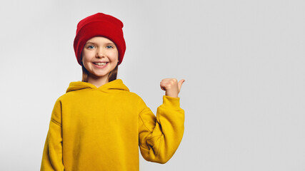 Trendy little girl, pointing on copy space for your advertising, has excited surprised happy expression, isolated on white background