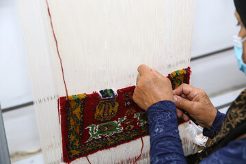 The carpet weaver puts a mask on her mouth. weaving and manufacturing of handmade carpets closeup....