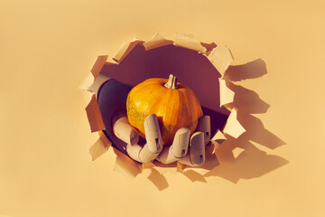 Orange pumpkin in wooden model hand through paper hole in torn beige paper. Hello Autumn season...