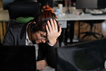 Portrait of woman in headset in frustration holds hands by face in office.