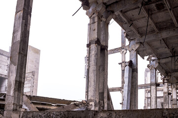A row of huge concrete piles in a row of the frame of a destroyed building against a gray sky in a...