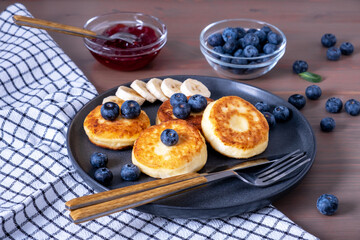 Cottage cheese pancakes, curdish pancakes, syrniki with fresh berries and banana, jam, sour cream for breakfast. Selective focus.