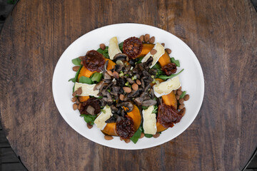 Healthy food and nutrition. Top view of a gourmet salad with arugula, roasted pumpkin, almonds, brie cheese, sun dried tomatoes and mushrooms. 