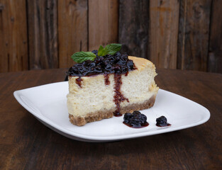 Desserts. Closeup view of a slice of Cheesecake with mascarpone cheese and berries dressing, in a white dish on the wooden table. 