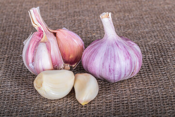 natural seasoning for the dish. garlic head and clove. there is burlap on the textured fabric. close-up