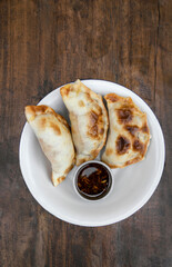 Finger food. Closeup view of three meat empanadas with chimichurri spicy sauce in a white bowl on the wooden table.