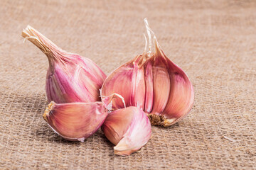 natural seasoning for the dish. garlic head and clove. there is burlap on the textured fabric. close-up
