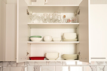 Fototapeta na wymiar Open white kitchen cabinet door with white dishes inside