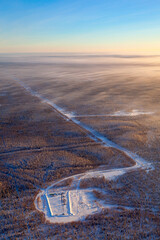 Pump jack and wellhead in the oilfield situated in the endless spaces of the winter forest, air photo