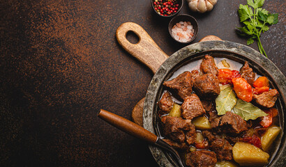 Delicious beef meat stew dish with potatoes, carrot and gravy in rustic metal bowl with spoon,...