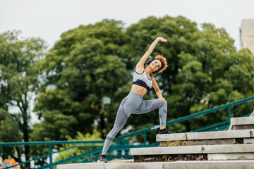 A happy, fit sportswoman listening to music and stretching on the stairs on the street. A sportswoman workout outdoors