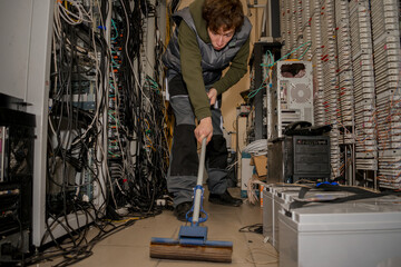 A young guy washes the floor with a mop in the server room. A technician is cleaning up the data...