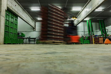 Naklejka premium A forklift on the move. Warehouse and warehouse for packaging and stocks of goods. Forklifts is in an empty warehouse, in the background are boxes and pallets for packing fresh fruits and vegetables