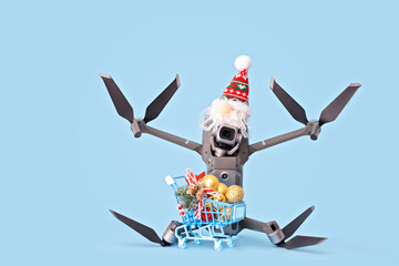 Drone in Santa's cap and a trolley cart with festive Christmas decor on the light blue background. Creative Christmas concept