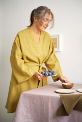 Obraz premium Young girl in a dressing gown lays the table. Natural fabrics and materials around. Cozy home. Side view.