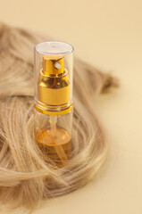 Obraz premium oil in a bottle with a dispenser and blonde hair on a beige background