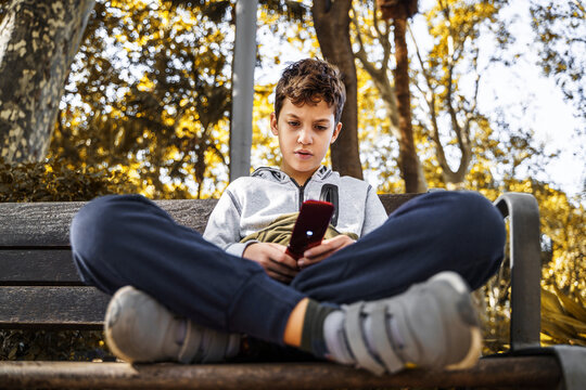 Kid sitting on a bench watching message on an outdated gsm cellphone
