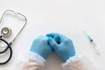Fototapeta premium hands of young doctor in protective suit and blue protective gloves on table next to stethoscope and syringe for injecting vaccine