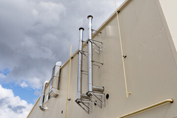 Metal ventilation pipes on the outer wall of a beige industrial building against a blue sky...