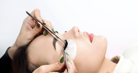 Eyelash extension procedure. The master uses tweezers to apply long eyelashes to beautiful female eyes.