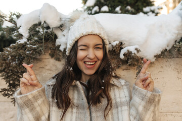 Close-up of cute caucasian girl winking and crossing her fingers outdoors on winter day. Brunette...