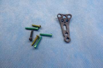 an explanted titanium plate and various titanium screws of a radius fracture lie on a blue support