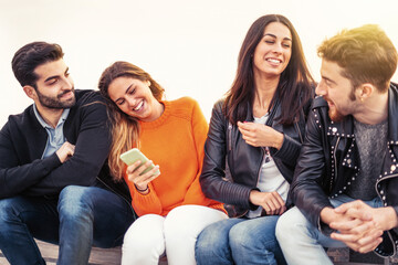 Group of young people having fun talking together and using smartphone sitting outdoors