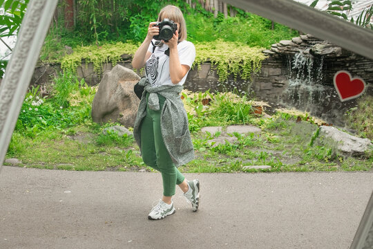 Woman photographer takes pictures of herself in the reflection of a large mirror, the mirror stands in a public place in the park during the warm season