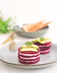 A plate  layer of beetroot napoleon and goat cheese appetizer in plate topped with sliced avocado, shape as French mille-feuille a healthy dish and ideal for diet