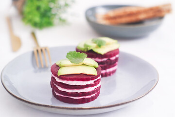  A plate of layer stack of beetroot napoleon and goat cheese appetizer in plate with sliced avocado, shape as French mille-feuille a healthy dish and ideal for diet