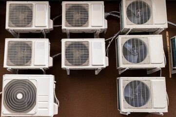 Many air conditioner compressors on the brown wall of the house