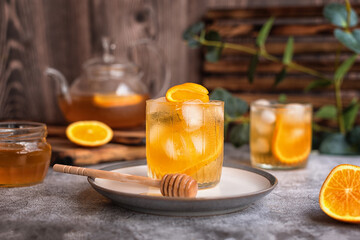 summer tea party: refreshing cold black tea with oranges and honey on a gray background