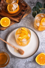 summer tea party: refreshing cold black tea with oranges and honey on a gray background