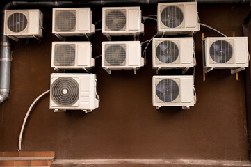 Many air conditioner compressors on the brown wall of the house