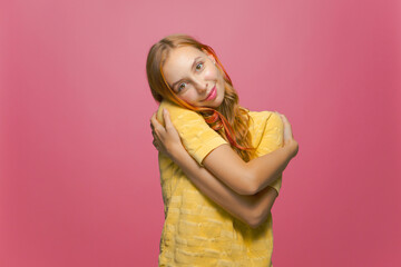 Beautiful young girl embracing herself smiling from pleasure on pink background. Self-love,...
