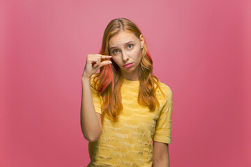 Disappointed girl showing small size with pity on pink studio background. Young woman showing...