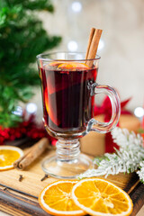 delicious hot spicy red mulled wine with orange and cinnamon spices near the Christmas tree with decorations and bokeh garlands