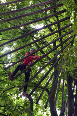 Teen boy crossing the suspension bridge in the rope summer park